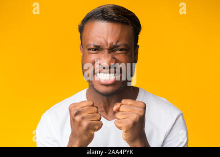 African American Guy Clenching pugni guardando la telecamera, sfondo giallo Foto Stock