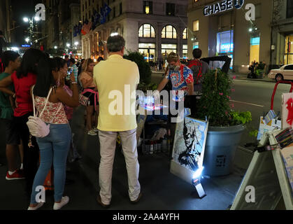 New York City, NY USA. Lug 2017. Giovane artista di strada per la verniciatura a spruzzo con artwork onlooking turisti e newyorkesi. Foto Stock