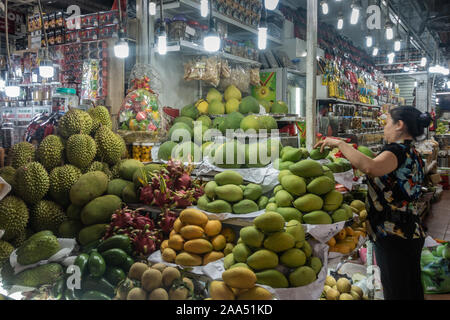 La città di Ho Chi Minh, Vietnam - Marzo 12, 2019: Downtown. Donna organizza i mucchi di frutta diversa presso il suo stand al coperto Ben Tanh mercato. Abbondanza di l Foto Stock