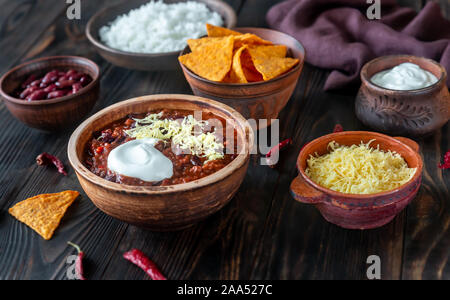 Ciotola di chili con carne con condimenti su un tavolo di legno Foto Stock