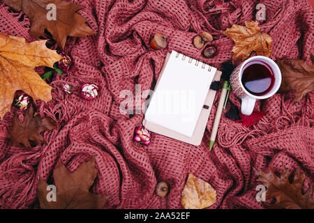 Composizione d'autunno. Tazza di tae, blanket, notebook con penna, autunno foglie essiccate e acorn. Appartamento laico, vista dall'alto, spazio di copia Foto Stock