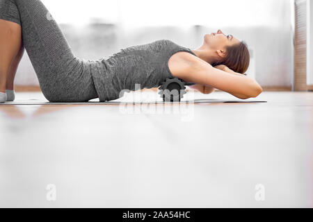 Ragazza fare yoga giacente sul massaggiatore sul tappeto grigio in palestra durante il giorno. Foto Stock