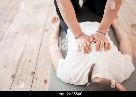 Uomo Donna di massaggio alla schiena in T-shirt bianco giacente sul tappeto grigio in palestra Foto Stock