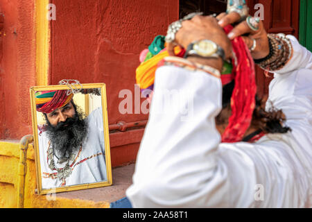 Sono un uomo guarda il suo riflesso in uno specchio quando occupare il suo turbante, Jodhpur, Rajasthan, India Foto Stock