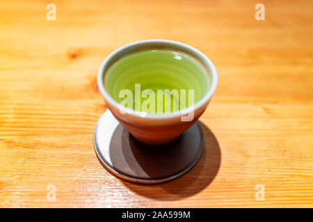 Macro di primo piano di una piccola tazza con vibrante giapponese del tè verde sencha di colore sul tavolo di legno con coaster Foto Stock