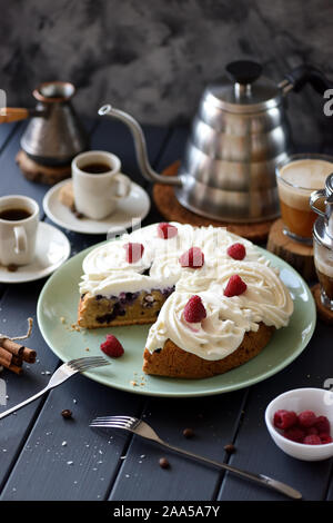 Torta alla frutta con crema di cocco rose e lamponi servita con caffè nero su sfondo grigio scuro copia spazio. Ancora in vita con illuminazione naturale Foto Stock