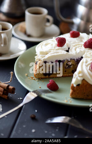 In casa mirtillo torta con crema di cocco rose e lamponi servita con caffè su sfondo scuro. Ancora in vita con illuminazione naturale scena Foto Stock