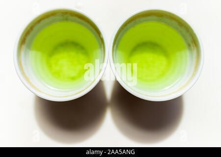 Lato superiore piatto vista laici verso il basso delle piccole due tazze riempite con il Giapponese vivace giallo verde Sencha tè genmaicha colore per la prima colazione o la cerimonia Foto Stock