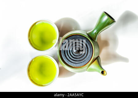 Parte superiore piatta della teiera kyusu e piccolo due tazze riempite con il Giapponese vivace giallo verde sencha fukamushi o genmaicha tè colore contro uno sfondo bianco Foto Stock