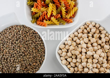 Tre bianchi ciotole con legumi come lenticchie e ceci e pasta con verdure colorate Foto Stock