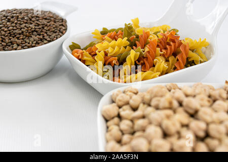 Vista ravvicinata di pasta colorata, i ceci e le lenticchie in ciotole di colore bianco su sfondo bianco Foto Stock