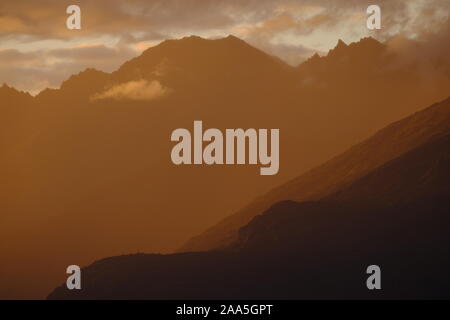 Drammatico tramonto arancione luce dal sole di mezzanotte sulle vette del Knik River Valley, Chugach Mountains, centromeridionale, Alaska Foto Stock