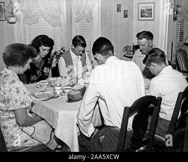 Circa: fine degli anni cinquanta o inizi degli anni sessanta - La famiglia di un camionista vive una vita simile a quella di altri lavoratori americani. Questa famiglia di Arlington Virginia bow le loro teste in preghiera prima di mangiare il loro pasto serale. Foto Stock