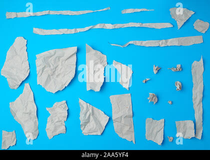 Set di vari pezzi di grigio strappato carta sgualcita su uno sfondo blu, close up Foto Stock