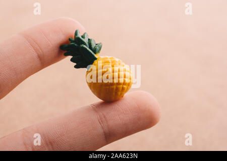 Mano che tiene un piccolo ananas miniatura su uno sfondo sul display Foto Stock