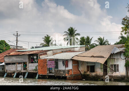 In Cai Be, il Delta del Mekong, Vietnam - Marzo 13, 2019: lungo quello dei Kinh 28 canal. Riga di baraccopoli-come povere case costruite su palafitte e sulla riva con lamiera grecata pl Foto Stock