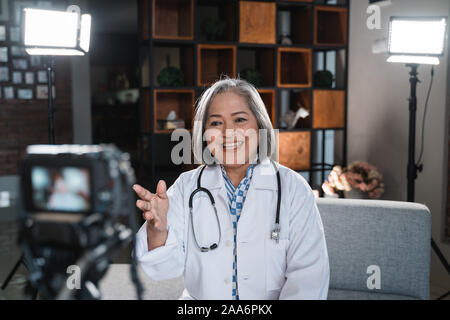 Saluti senior medico donna per registrare un video del suo blog Foto Stock