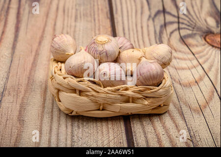 A pochi capi di giovani aglio in un cesto di vimini su un sfondo di legno. Raccolto autunnale. L'agricoltura moderna. Close up Foto Stock