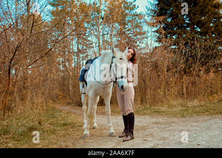 Ragazza in sella ad un cavallo bianco nel bosco Foto Stock