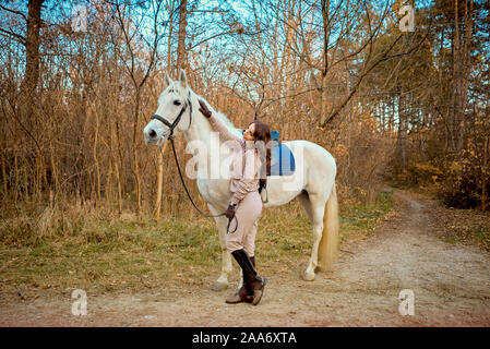 Ragazza in sella ad un cavallo bianco nel bosco Foto Stock