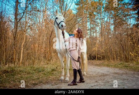 Ragazza in sella ad un cavallo bianco nel bosco Foto Stock