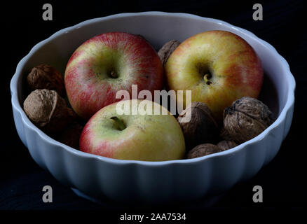 Apple e le noci intere in un bianco coppa di frutta contro uno sfondo nero Foto Stock