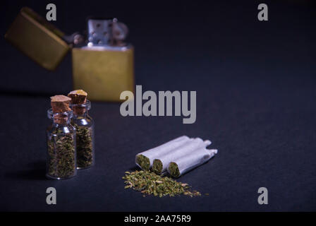 Un uomo fuma cannabis erbaccia, di un giunto e un accendino nelle sue mani. Il fumo su uno sfondo nero. Concetti di marijuana medica uso e legalizzazione del Foto Stock