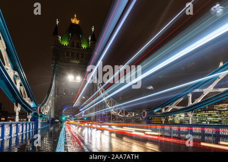 London, England, Regno Unito - 15 Novembre 2019: il traffico si sfoca in percorsi di luce su una notte piovosa il Tower Bridge di Londra. Foto Stock