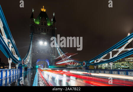 London, England, Regno Unito - 15 Novembre 2019: il traffico si sfoca in percorsi di luce su una notte piovosa il Tower Bridge di Londra. Foto Stock
