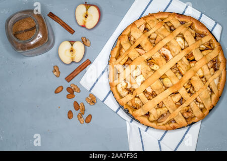 La torta di mele sul grigio di un asciugamano da cucina, con mele, cannella, zucchero e i dadi, vista dall'alto Foto Stock