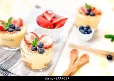 In casa, squisiti dessert Tiramisu' in vetri decorati con fragola, mirtillo, menta bianca sul tavolo di legno, Foto Stock