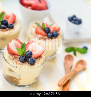 In casa, squisiti dessert Tiramisu' in vetri decorati con fragola, mirtillo, menta bianca sul tavolo di legno, Foto Stock