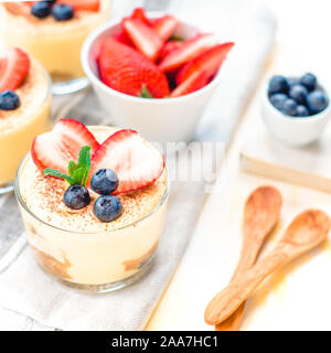 In casa, squisiti dessert Tiramisu' in vetri decorati con fragola, mirtillo, menta bianca sul tavolo di legno, Foto Stock