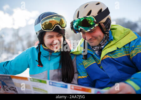 Donna sorridente e uomo nel casco con la mappa in mani alla neve località sulla giornata invernale Foto Stock