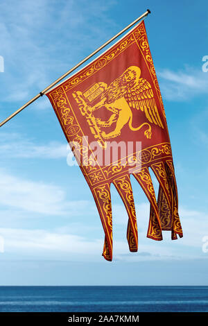 Close-up di una bandiera della città di Venezia e del Veneto con il leone alato di San Marc (San Marco) su un cielo blu con nuvole e mare. Italia Foto Stock