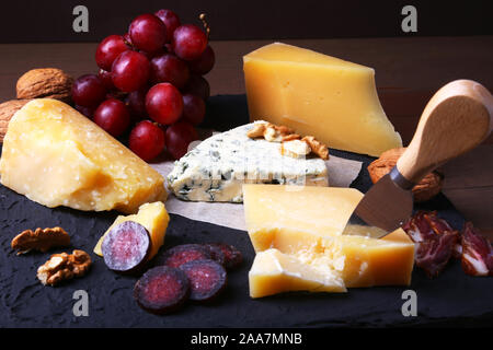 Formaggi assortiti, noci, uva, frutta, carne affumicata e un bicchiere di vino su un serving table. Dark e Moody stile. Spazio libero per il testo Foto Stock