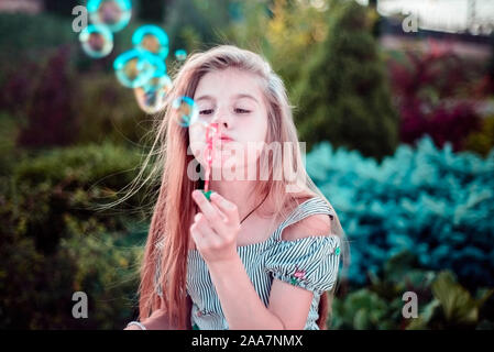 Ritratto di una bellissima bambina soffiando bolle di sapone. Un bambino gioca con bolle, su uno sfondo verde. Per esterno Foto Stock