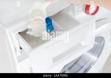 Il detersivo in polvere e detergente in una tazza e mano womans, lavatrice, il fuoco selettivo Foto Stock