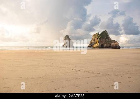 Vista sulle famose rocce di Wharariki Beach nella Baia Dorata in Nuova Zelanda durante il tramonto con nuvole drammatico. Orme nella sabbia in primo piano. Foto Stock