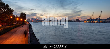 Un uomo cammina lungo la Woolwich Thames di Fiume percorso al tramonto con lo skyline di Docklands e Silvertown dietro. Foto Stock