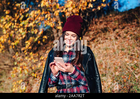 Giovane donna writting sms sul cellulare in autunno park. Foto Stock