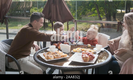 La famiglia in una caffetteria sulla terrazza. Papà e Mamma a giocare con i bambini con le palme Foto Stock