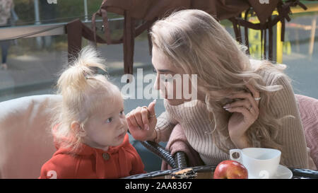 La famiglia in una caffetteria sulla terrazza. Mom gioca con la sua piccola figlia, bacia il Foto Stock