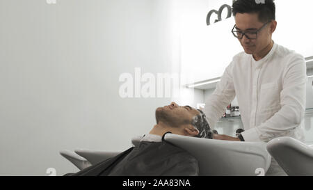 Parrucchiere uomo Asian lava la testa di un client Foto Stock
