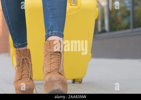 Close-up delle gambe di una signora traveler con una valigia gialla, sta camminando per la strada dall'hotel. Foto Stock