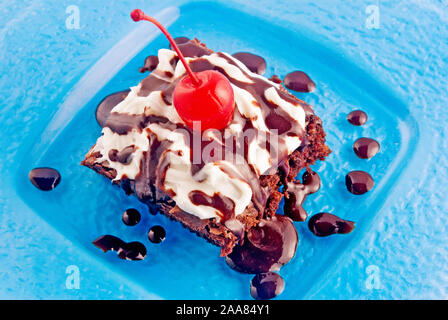 Cioccolato artigianale fudge brownie conditi con panna montata e ciliegie al maraschino. Servita in un colorato blue plate. Foto Stock