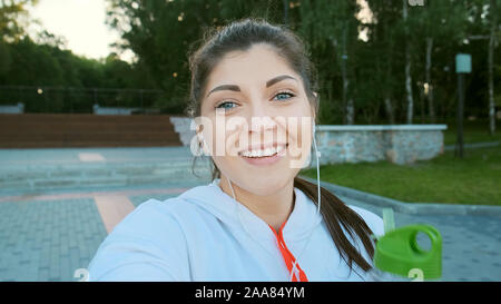 POV giovane donna blogger in una felpa sportiva è la registrazione di un video per vlog prima di jogging. Ella parla e contiene una bottiglia di acqua Foto Stock