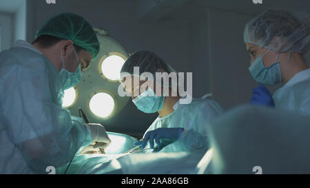 Due dei chirurghi al lavoro. L'infermiera dà al medico strumenti medicali. Foto Stock