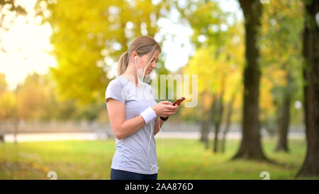 Ragazza atleta a fare jogging nel parco di sera. Piano di appoggio e di conversazione sulle reti sociali. Ascolto di musica. Allenamento. Uno stile di vita sano. Foto Stock