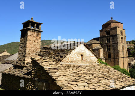 Tetto con camino tradizionale e la chiesa di Santa Maria, Santa Cruz de la Seros. Huesca. Aragona, Spagna Foto Stock